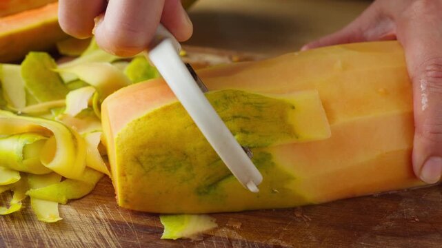 Peeling a ripe papaya with a vegetable peeler on a wooden cutting board