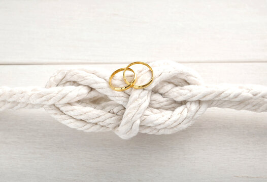 Golden wedding rings placed on a knotted white rope surface