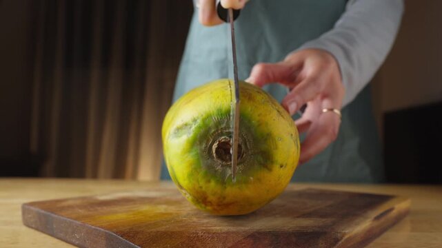 Person cutting a ripe papaya in half on a wooden cutting board
