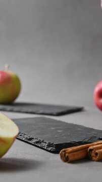 Hand lifts apple cider cold brew tonic from slate board beside fresh apples and cinnamon sticks.