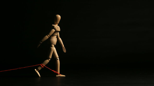 Wooden mannequin trying to walk forward while its feet are tied back by a red string, symbolizing limitation, restriction, or being held back.