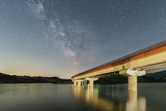 View of Lago di Cingoli at night with the Milky Way galaxy visible in the starry sky above the bridge in Cingoli, Marche, Italy.