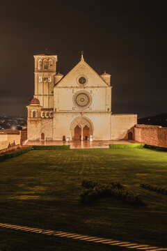 View of the Basilica of Saint Francis of Assisi illuminated at night with a manicured lawn in the foreground in Assisi, Umbria, Italy.