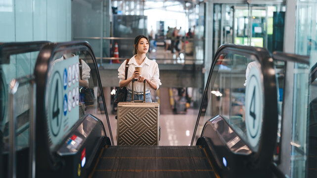 Young adult business asian woman to transit with travel luggage at international airport terminal on the go with financial freedom