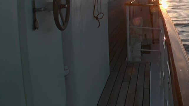 The scene shows ship hull and wooden deck edge in open sea beside sunlit water. The view includes ship hull and narrow wooden deck edge beside rippled sea water with warm sunlight reflection.