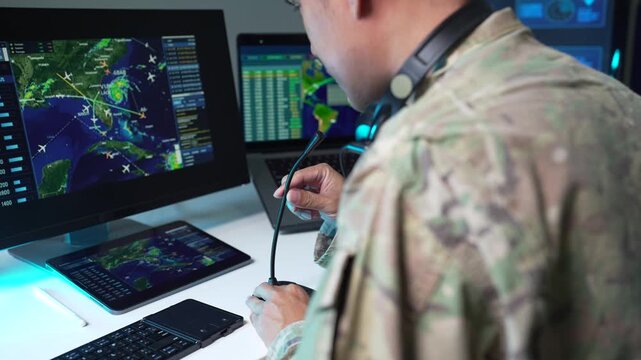 adult asain male soldier wearing headset typing on computer in military command center.