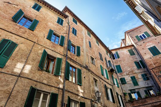 View of historic brick buildings with traditional green shutters in the narrow streets of the old town in Siena, Tuscany, Italy.