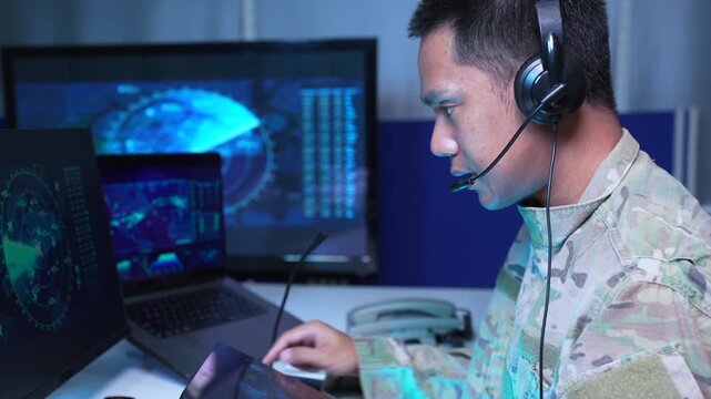 adult asain male soldier wearing headset typing on computer in military command center.