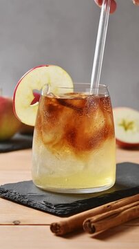 Glass straw stirs apple cider cold brew tonic, blending coffee layers with ice in closeup glass.