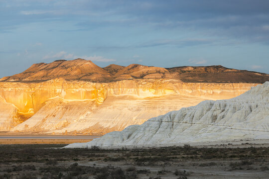 View of the dramatic white chalk cliffs and golden rock formations of the Tuzbair salt flats under a clear blue sky in the desert landscape of Mangystau District, Mangystau Region, Kazakhstan.