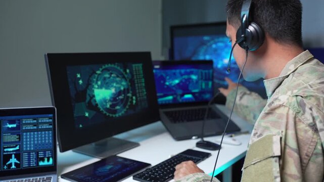 adult asain male soldier wearing headset typing on computer in military command center.