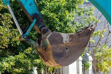 Blue excavator bucket hangs suspended in lush green foliage © schankz