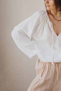 Stylish woman in relaxed white shirt and beige bottoms posing naturally against soft neutral background