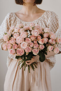Portrait of elegant lady in textured beige outfit posing with oversized pink flower bouquet