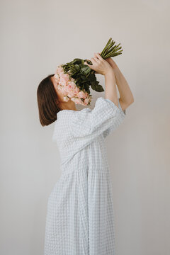 Young brunette embracing rose bouquet while wearing flowing dress