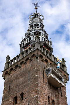 View of the historic brick tower of the Grote Kerk with its ornate spire and clock against a blue sky in Monnickendam, North Holland, Netherlands.