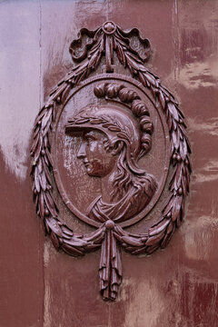 View of a detailed relief carving of a Roman soldier in profile, framed by an ornate laurel wreath on a glossy brown door in Monnickendam, North Holland, Netherlands.
