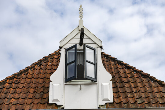 View of a traditional dormer window with black frames set into a red clay tiled roof in Monnickendam, North Holland, Netherlands.