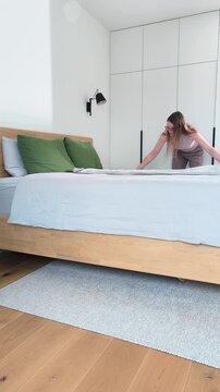 Making bed in bedroom during morning housekeeping routine. Young female arranges blankets. tidy lifestyle..