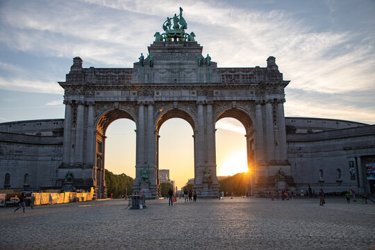 View of the Cinquantenaire Arch at sunset with people walking on the cobblestone square in Brussels, Brussels, Belgium.