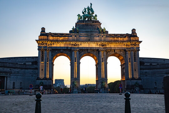 View of the illuminated Cinquantenaire Arch at sunset with cobblestone foreground in Brussels, Brussels, Belgium.