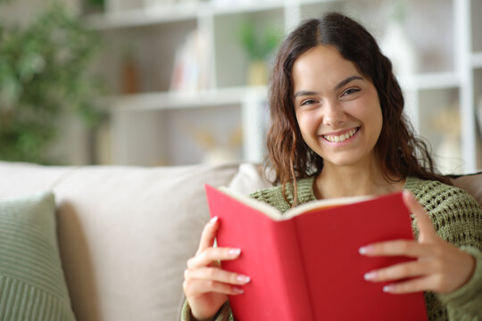 Happy young woman looking at you holding paper book