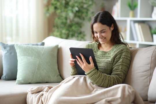 Happy young woman using tablet covered with a blanket in winter