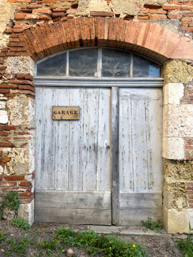 Weathered wooden garage door set in a round brick archway, Gers, Gimont, France