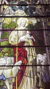 Historic stained glass church window depicting Jesus Christ as the Good Shepherd with sheep, colorful religious art, Gothic arch design, Christian heritage, sacred architecture and spiritual symbolism