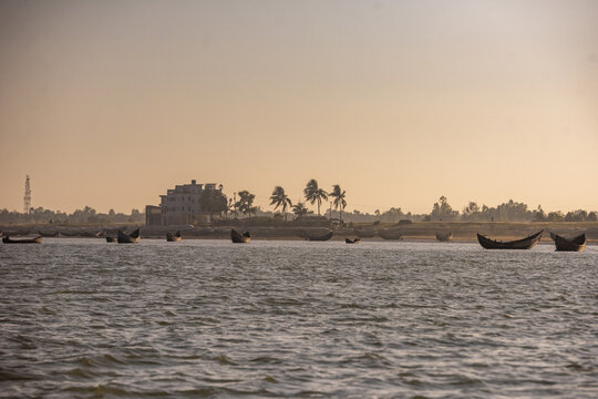 View of traditional wooden fishing boats on the river near the shoreline of Shah Porir Dwip with palm trees at sunset, Dakhinpara, Chittagong Division, Bangladesh.