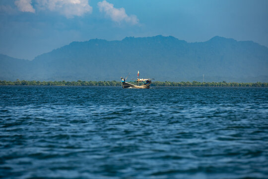 View of a small wooden boat on the calm waters of the Naf River with distant mountains under a clear blue sky at Naf River View Point, Cox's Bazar District, Chittagong Division, Bangladesh.