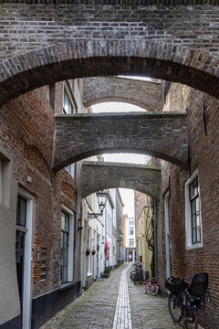View of a narrow cobblestone alleyway lined with historic brick buildings and connected by multiple brick arches in Kampen, Overijssel, Netherlands.