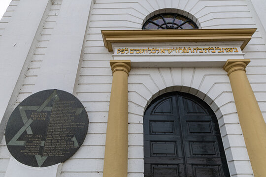 View of Joods Monument Kampen, a memorial plaque on a white building wall with yellow columns and a dark arched door in Kampen, Overijssel, Netherlands.