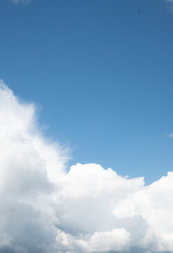 A vertical composition of a deep blue sky filled with heavy white clouds on the left and open space on the right. The bright daylight creates a calm and expansive atmosphere.