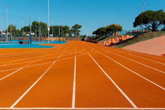 running track lanes red rubber surface white line markings athletics stadium empty bleachers clear blue sky outdoor field concept of sport, fitness, athletics
