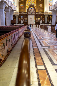 View of the interior of Saint Mark's Coptic Orthodox Cathedral with ornate marble flooring, wooden pews, and religious wall paintings in Cairo, Cairo Governorate, Egypt.