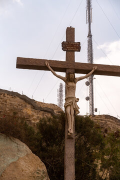 View of a wooden crucifix with a sculpture of Jesus Christ, set against a rocky hillside and a tall telecommunications tower in Coptic Cairo, Cairo, Cairo Governorate, Egypt.