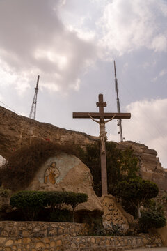 View of the large wooden cross and rock-carved relief of the Good Shepherd at the Monastery of Saint Simon set against a rocky cliffside in Cairo, Cairo Governorate, Egypt.