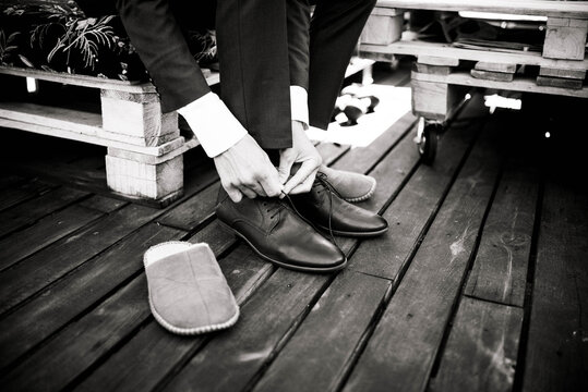 Black and white photo of a man tying shoelaces on wooden terrace