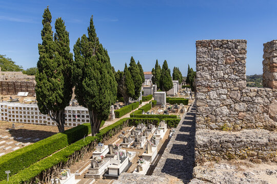 View of the cemetery inside the historic stone walls of Castelo de Santiago do Cacem, with rows of graves, hedges, and cypress trees in Santiago do Cacem, Setubal, Portugal.