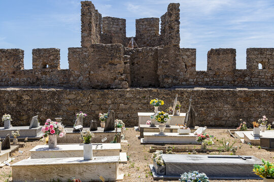 View of the historic Castelo de Santiago do Cacem featuring a cemetery with stone graves and colorful artificial flowers against ancient stone walls in Santiago do Cacem, Setubal, Portugal.