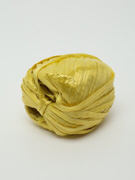 Ball of yellow raffia polypropylene ribbon for packaging and crafts on white background