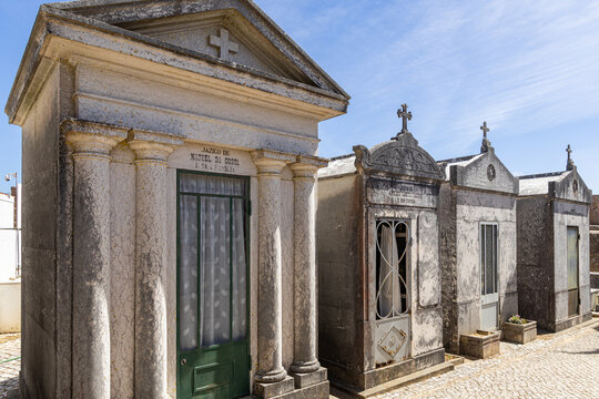 View of ornate stone mausoleums with classical columns and crosses in a historic cemetery in Santiago do Cacem, Setubal, Portugal.