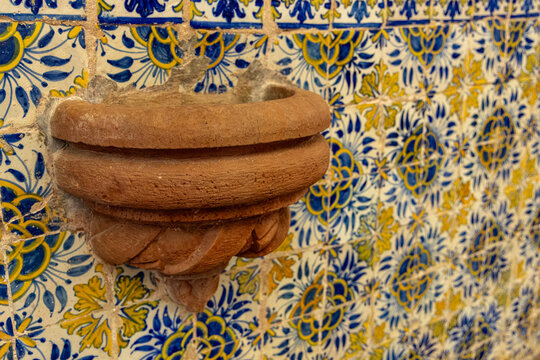 View of a terracotta stone basin mounted on a wall covered with traditional blue and yellow azulejo tiles inside the Igreja Matriz de Santiago do Cacem, Santiago do Cacem, Setubal, Portugal.