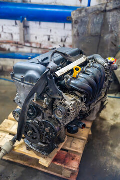 Removed car engine with intake manifold and alternator in auto repair workshop. Dismantled power unit represents engine replacement overhaul and used car repair