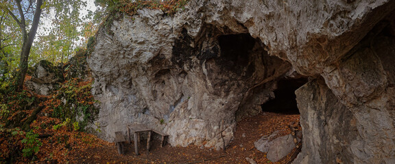 Rocky entrance and sheltered forecourt of Vidróczky Cave with a rustic wooden table, surrounded by autumn forest in the Bükk Mountains, northern Hungary. © Tibor