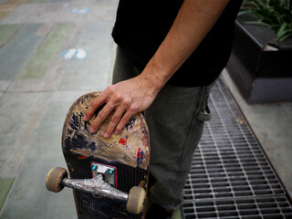 Hand of a male skateboarder wearing a black t-shirt with his skateboard on a cloudy day in Thailand © Windscale