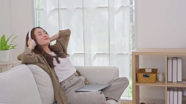 Woman with headphone on sofa using tablet in living room near window, home relaxation calm lifestyle, resting with audio during remote work break in bright cozy apartment interior