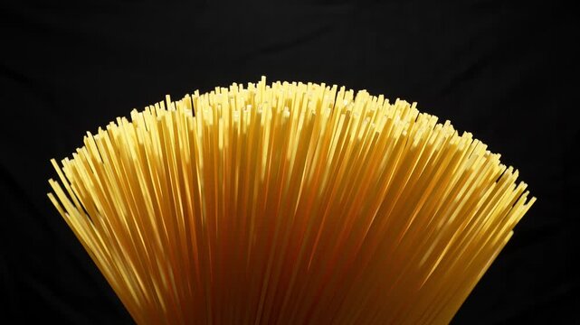 Cinematic low-angle close-up of raw spaghetti noodle bundle on black.