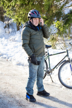 A senior man talks on his mobile phone beside his bicycle on an icy path in Helsinki, Finland, during winter commuting